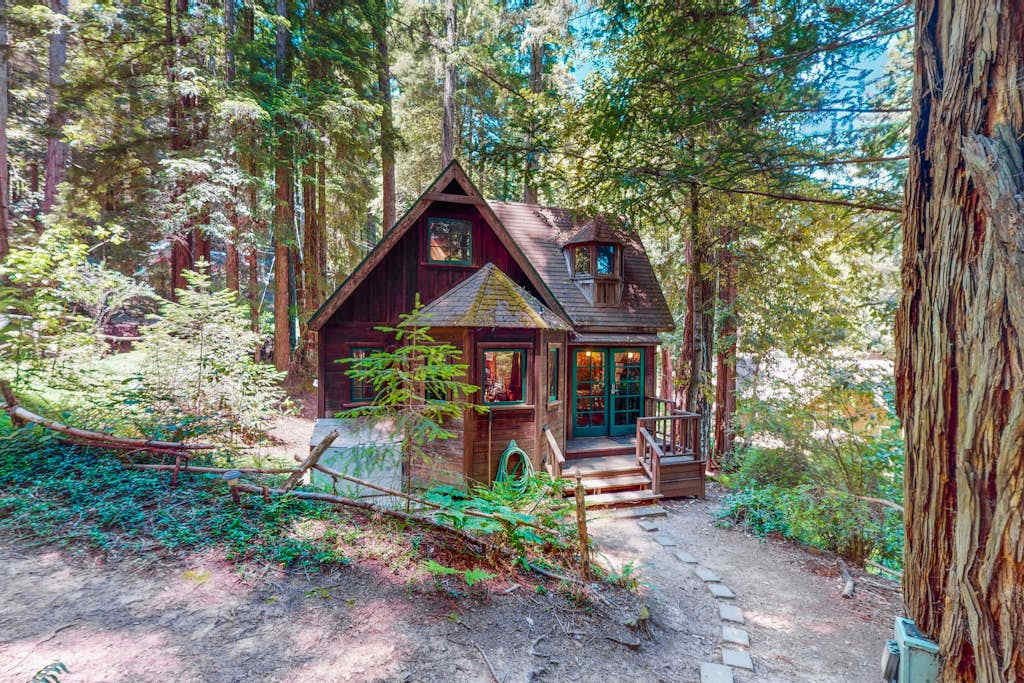 Tucked beneath towering Cazadero redwoods, your storybook cottage awaits — whimsical A-frame charm, warm wood siding, and a stone pathway leading to your private forest hideaway.