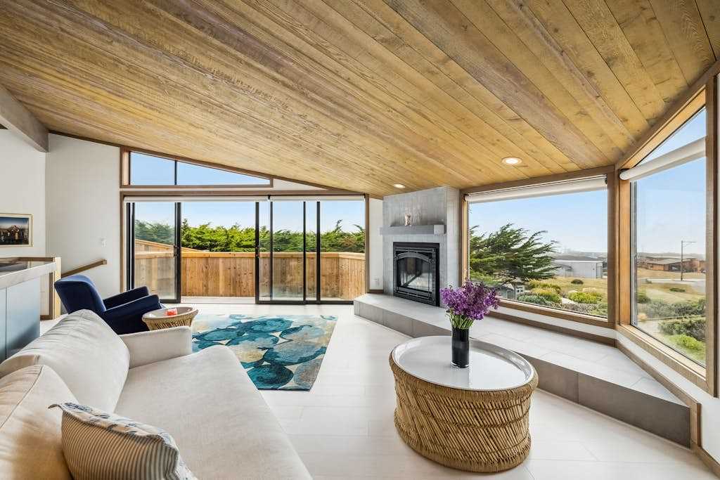Wraparound windows frame ocean peeks and cypress treetops from every corner of your light-filled coastal living room