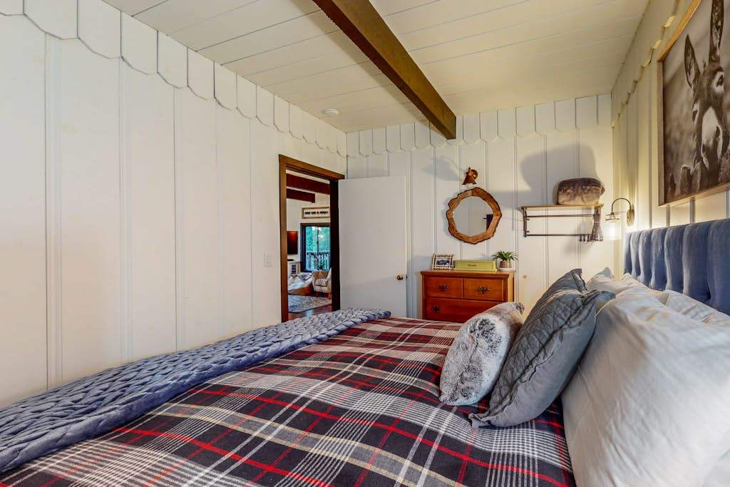 Wake to dappled forest light in your cabin bedroom — the plaid duvet, porthole mirror, and vintage dresser give The Lazy Bear its irresistible character.