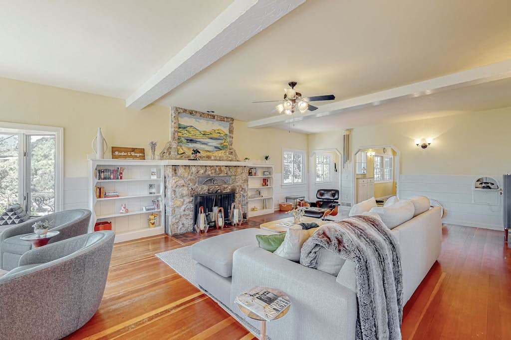 Sink into the sofa beside a striking stone fireplace in your Healdsburg cottage living room — hardwood floors, built-in shelves, and a ceiling fan keep every wine country evening comfortable.
