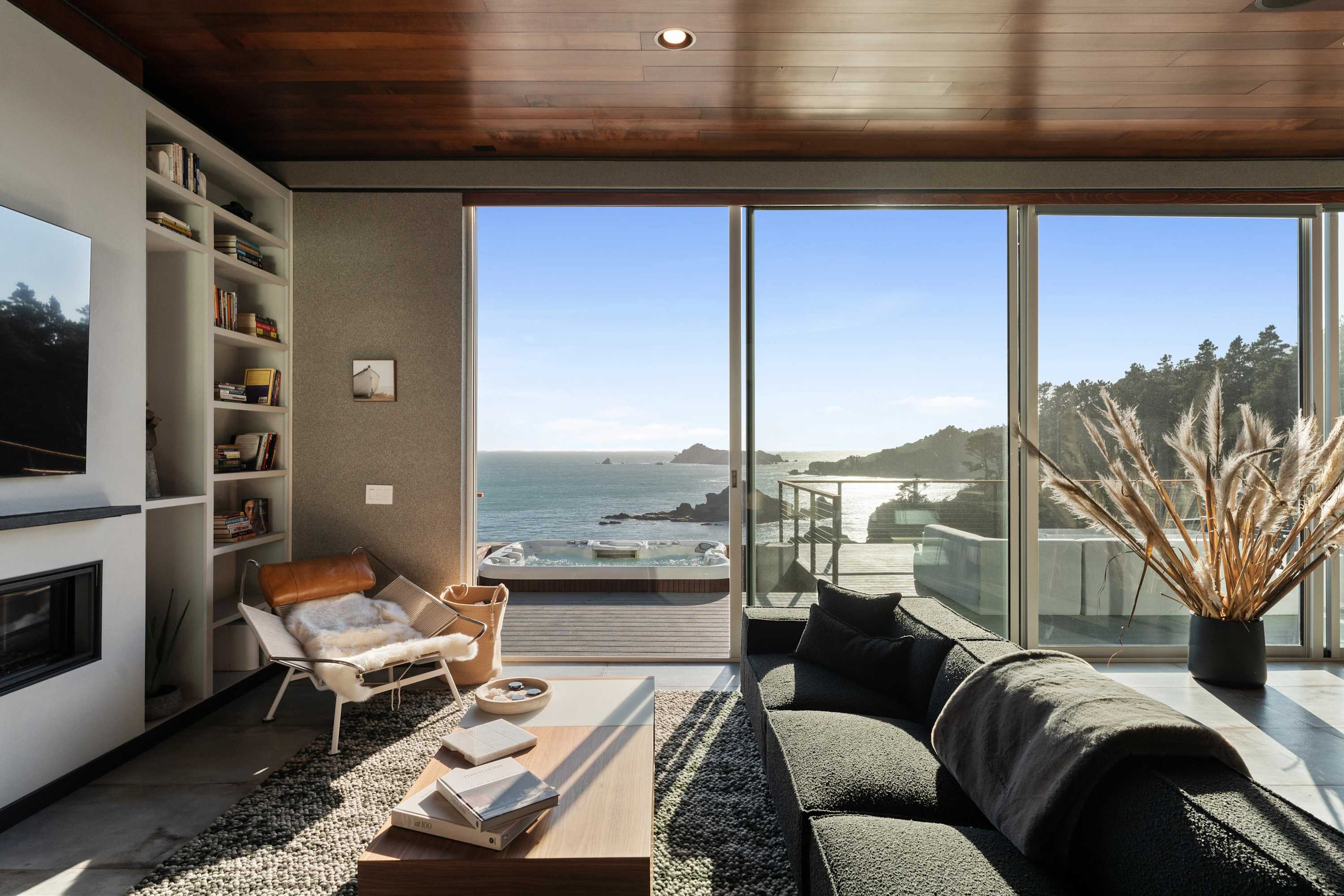 A reading chair by the fire, with the shelves behind and the cove through the sliders.