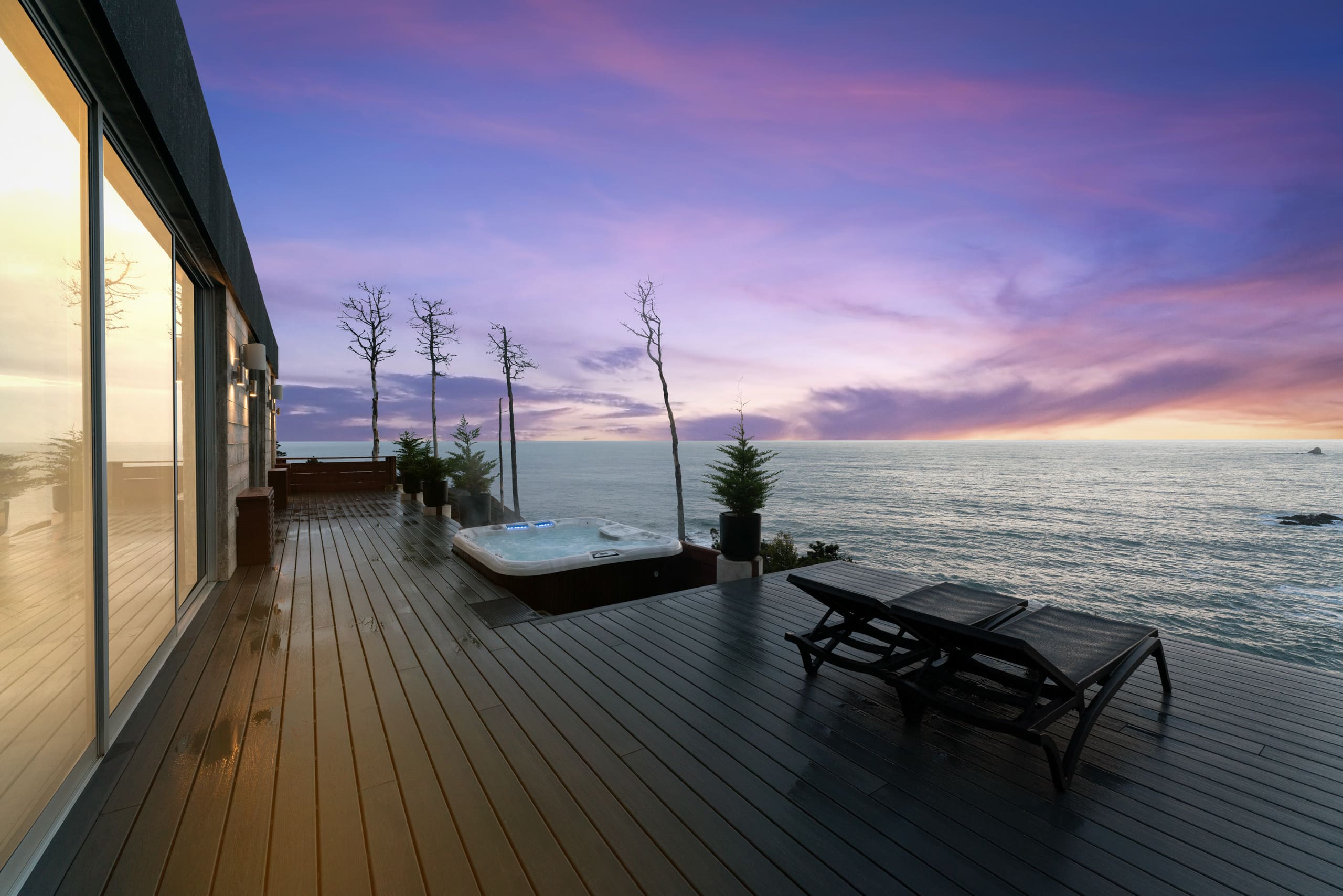 The deck at sunset: the hot tub and loungers along the rail, with the rock islands going dark offshore.