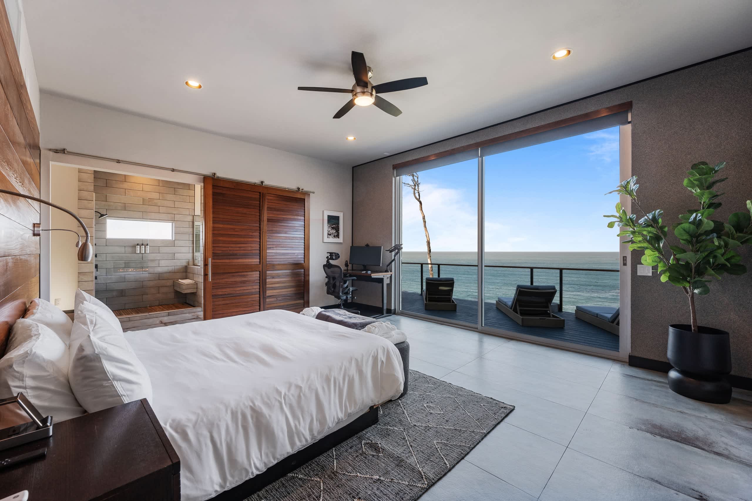 The primary suite looking toward the deck, with the fireplace wall at left and the cove through the sliders.