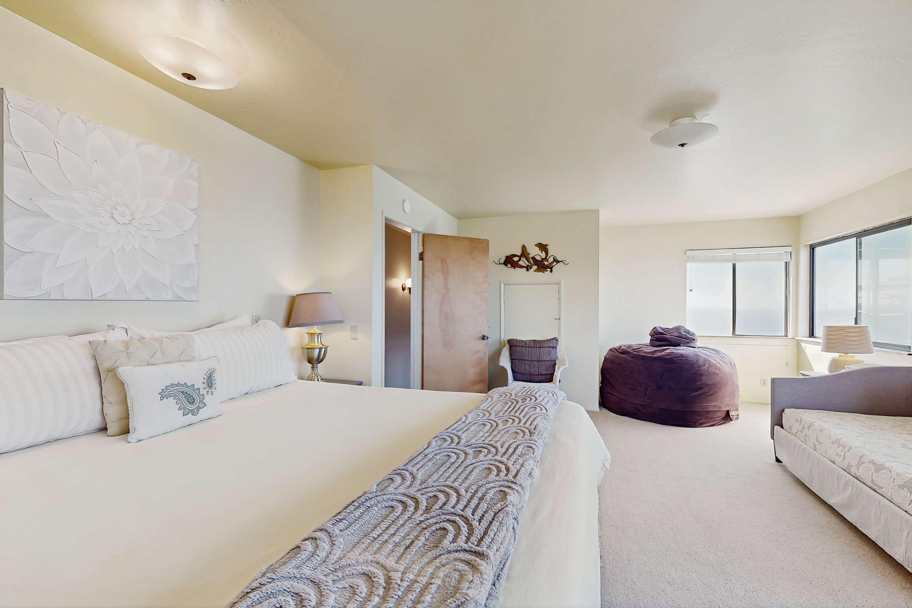 The spacious upper primary suite features a king bed, ocean views through the corner windows, and a cozy reading nook with a daybed.