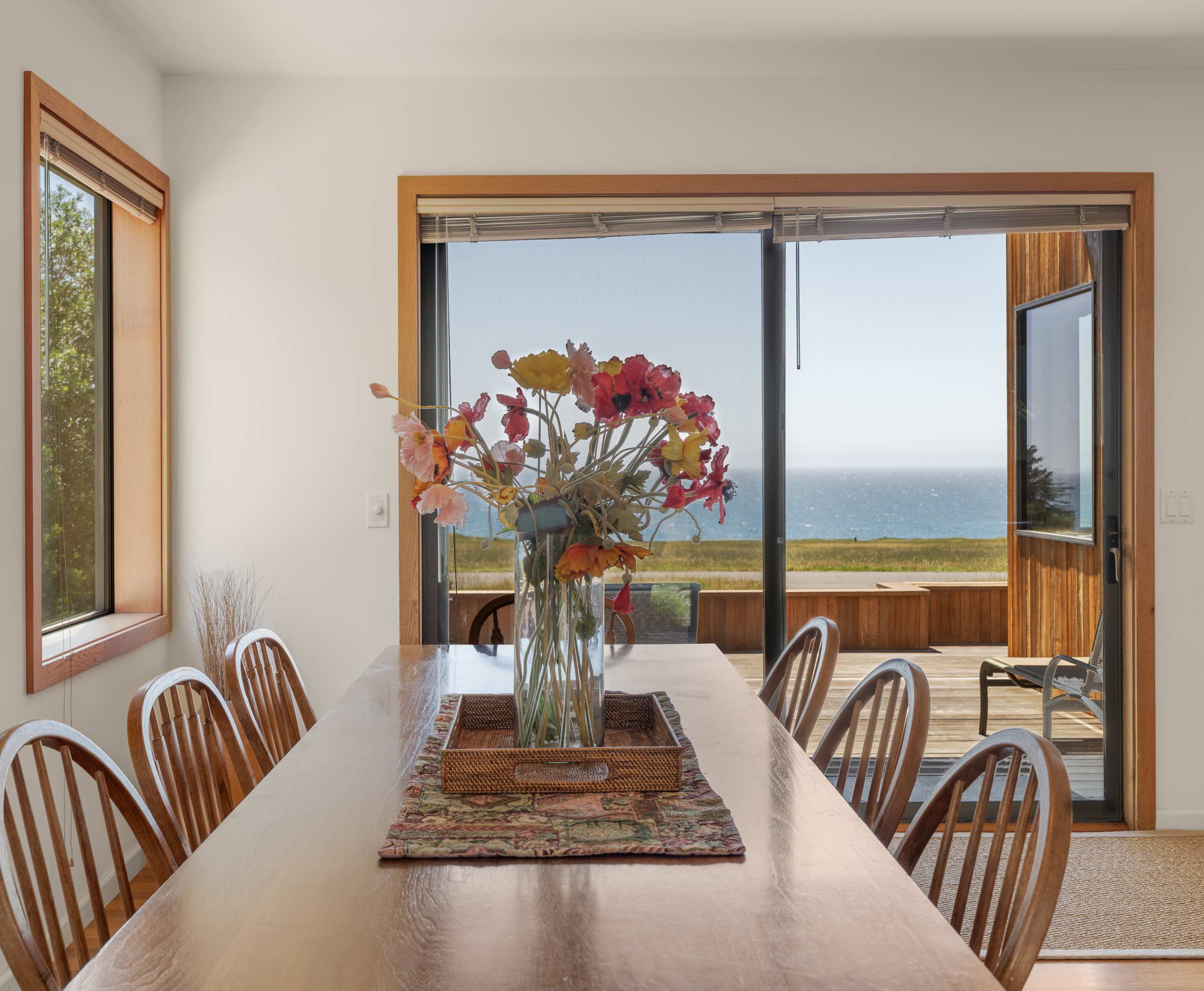 Dinner at the long table with the slider open — ocean breeze, the smell of nearby cypress, and the rolling hush of waves on the bluff below.