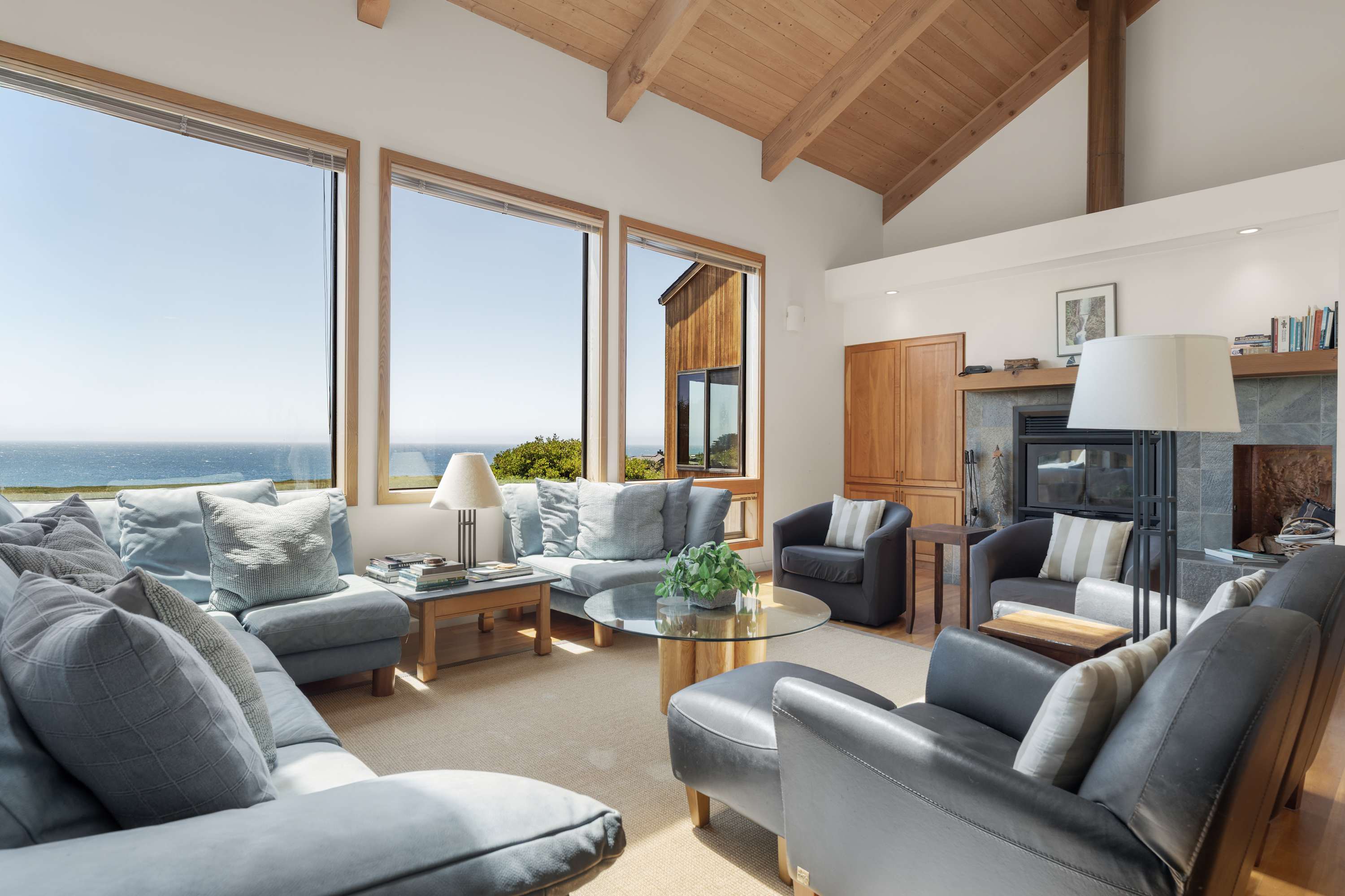 Vaulted wood beams stretch over the Pacific as you sink into the sectional — fireplace lit, fog rolling past your floor-to-ceiling windows.