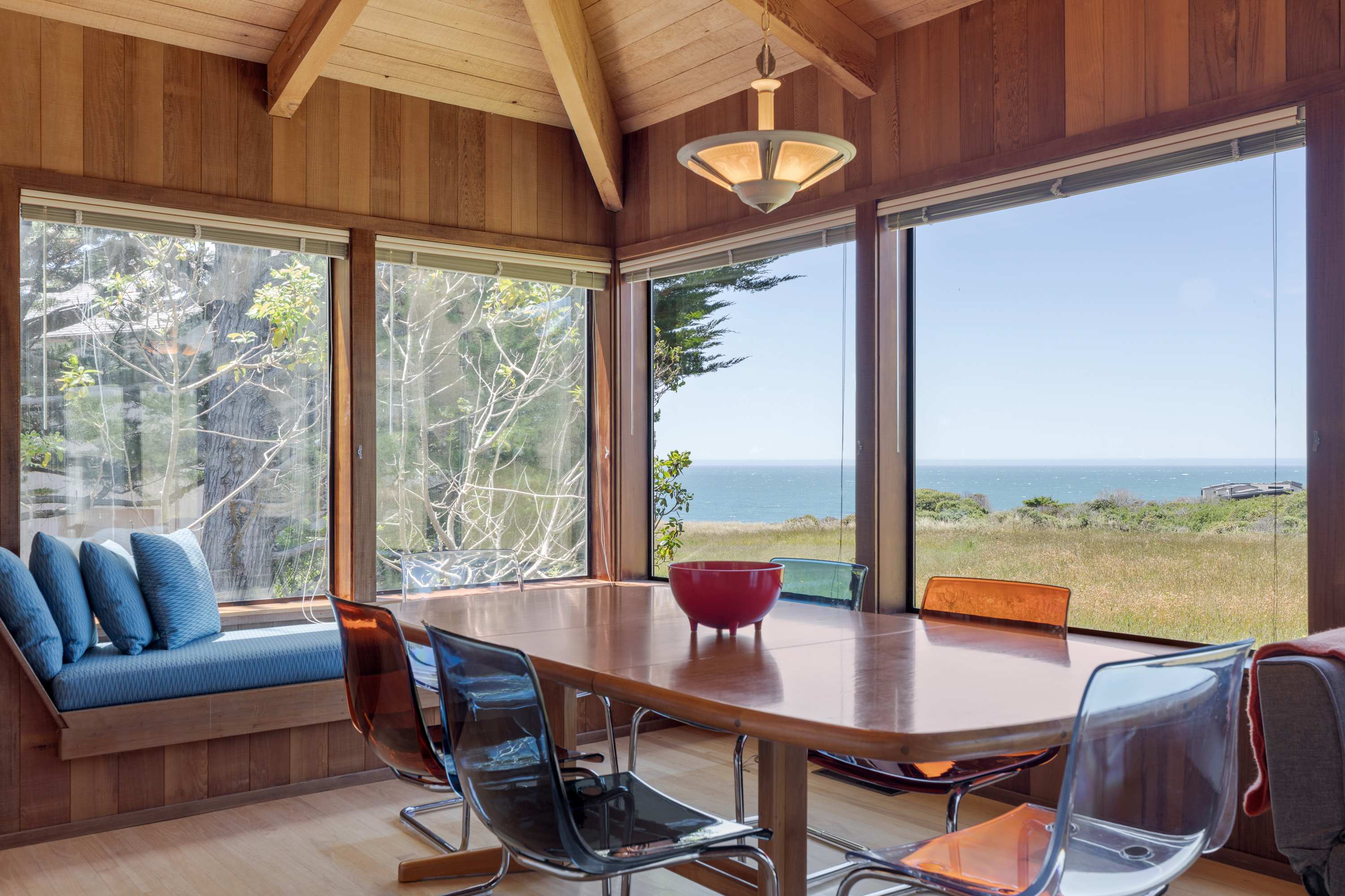 Sunlit dining nook with vaulted wood ceilings, a built-in window seat, and panoramic ocean views through expansive picture windows.
