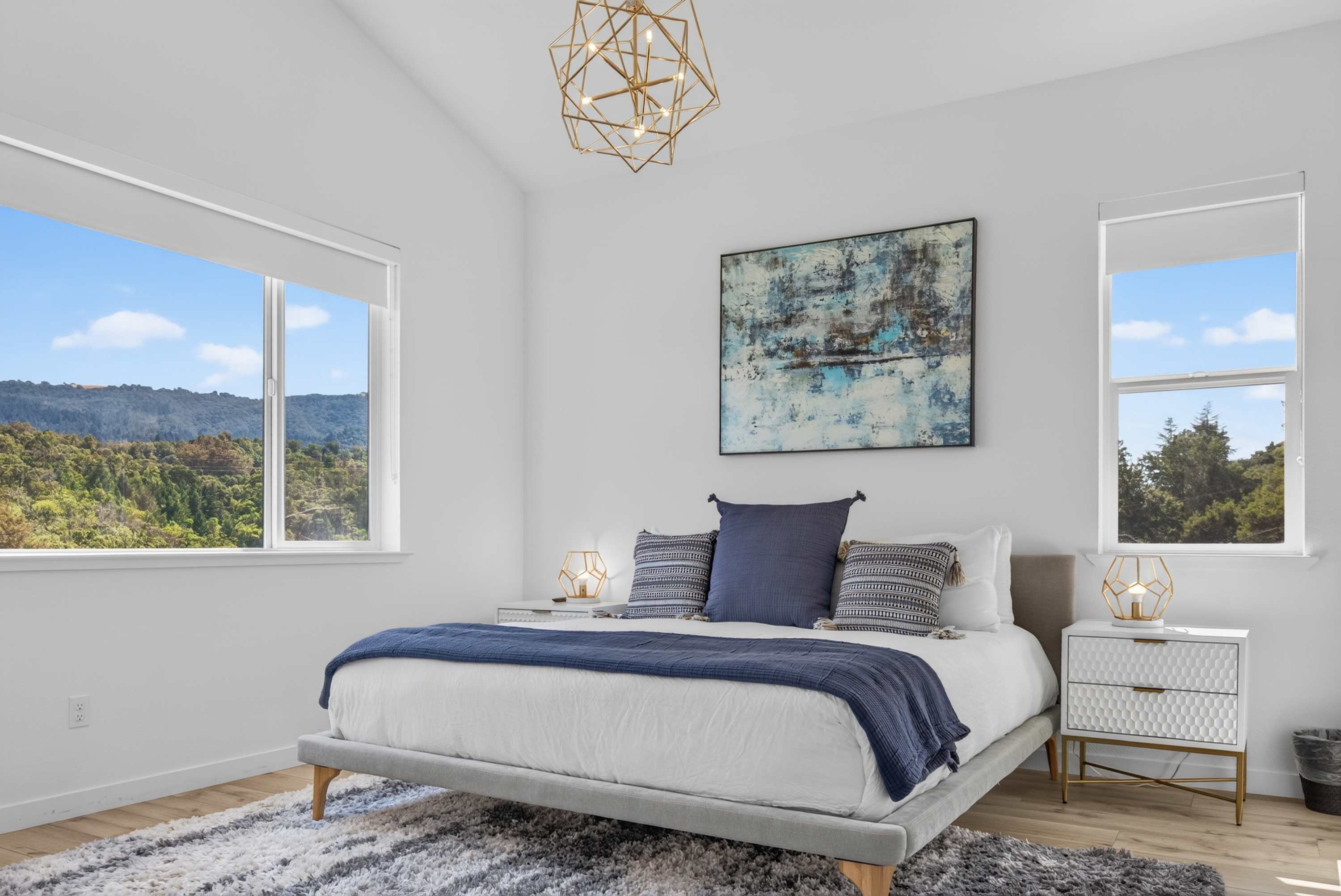 Wake to hillside views from both windows in this vaulted bedroom, where a brass geometric chandelier crowns the king bed.