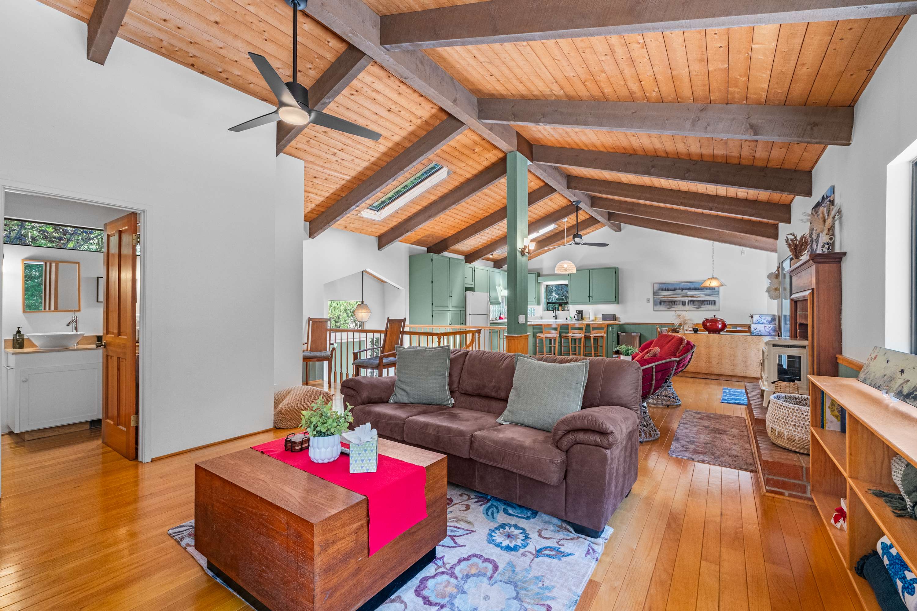 Gather under exposed beams in the open living-kitchen-dining flow, with the sage kitchen and electric warmth by the decorative brick hearth.