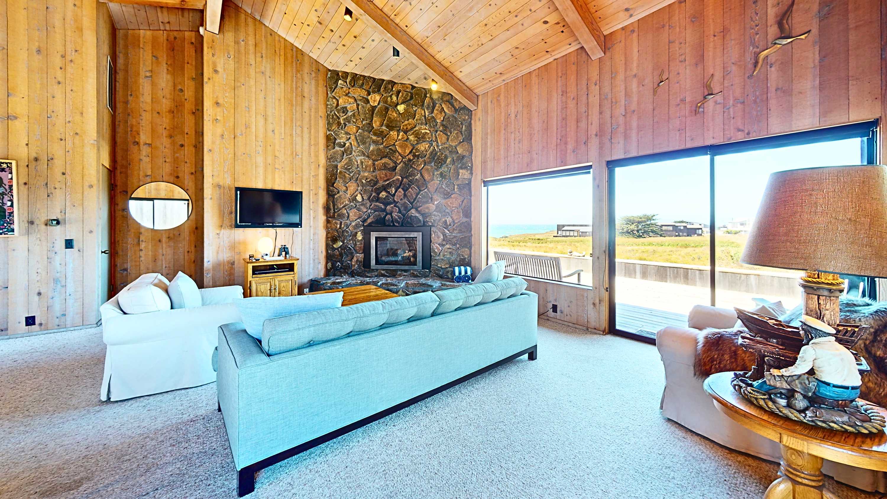 Settle in by the floor-to-ceiling stone fireplace — vaulted wood ceilings and sliding doors open to meadow and ocean views.