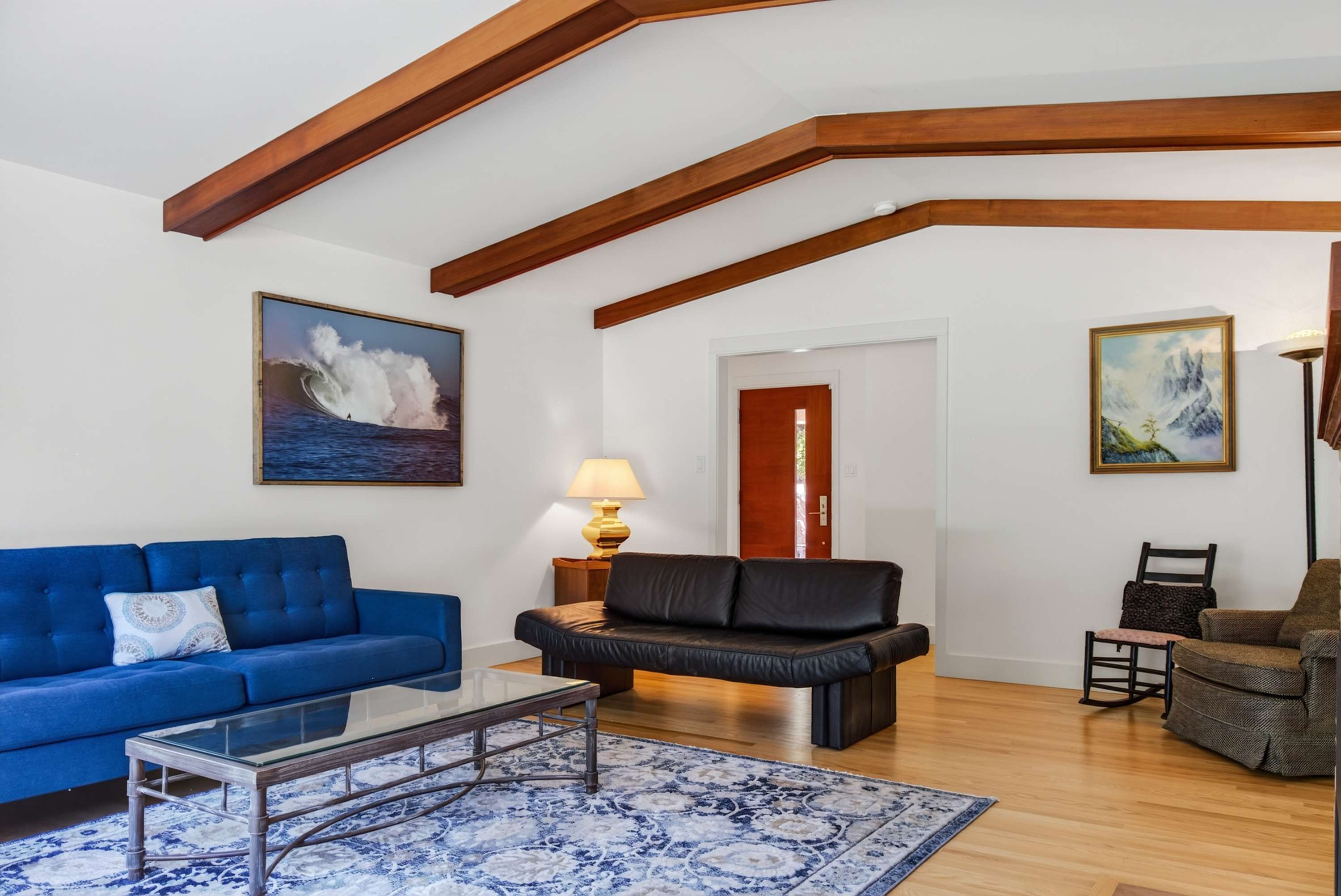 Gather around the glass coffee table in this airy living room — cobalt velvet sofa, black leather seating, and warm light from every angle.