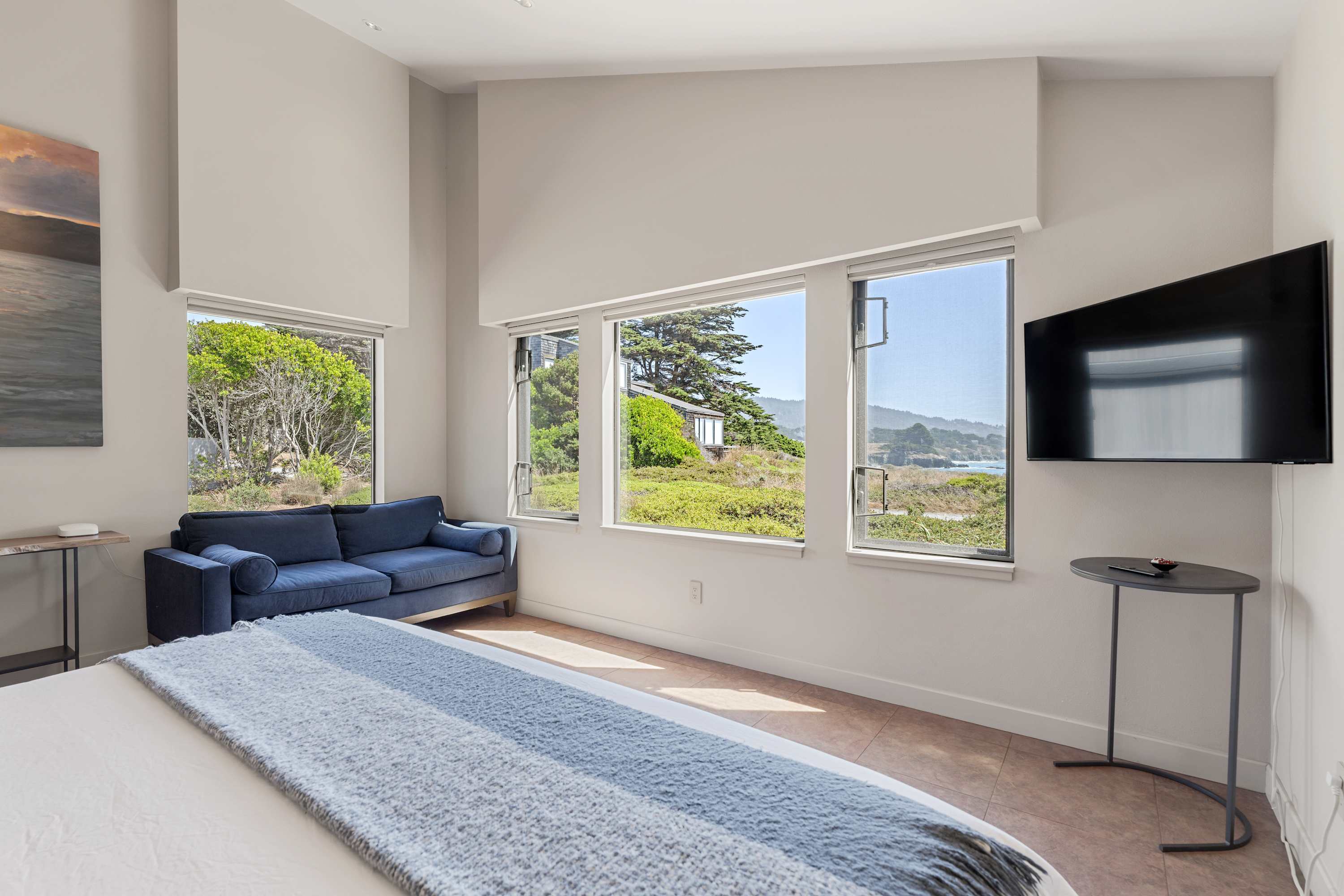 You wake to scrub and a thin line of sea. Navy loveseat under the window. A wool throw still at the foot of the bed.