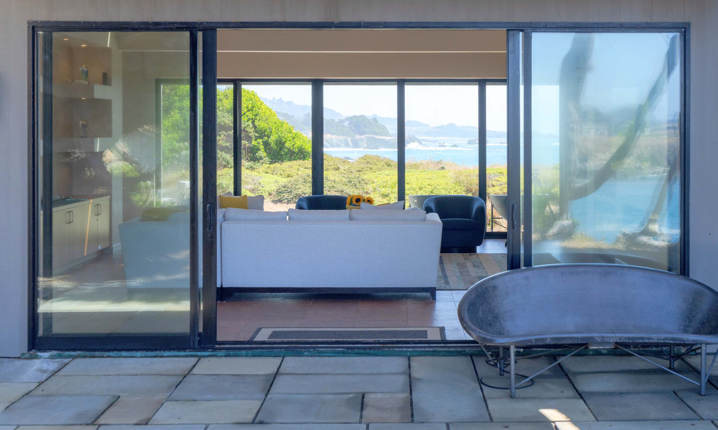 From the patio the house opens straight through — stone underfoot, then sofa, then nothing but cove and sky.