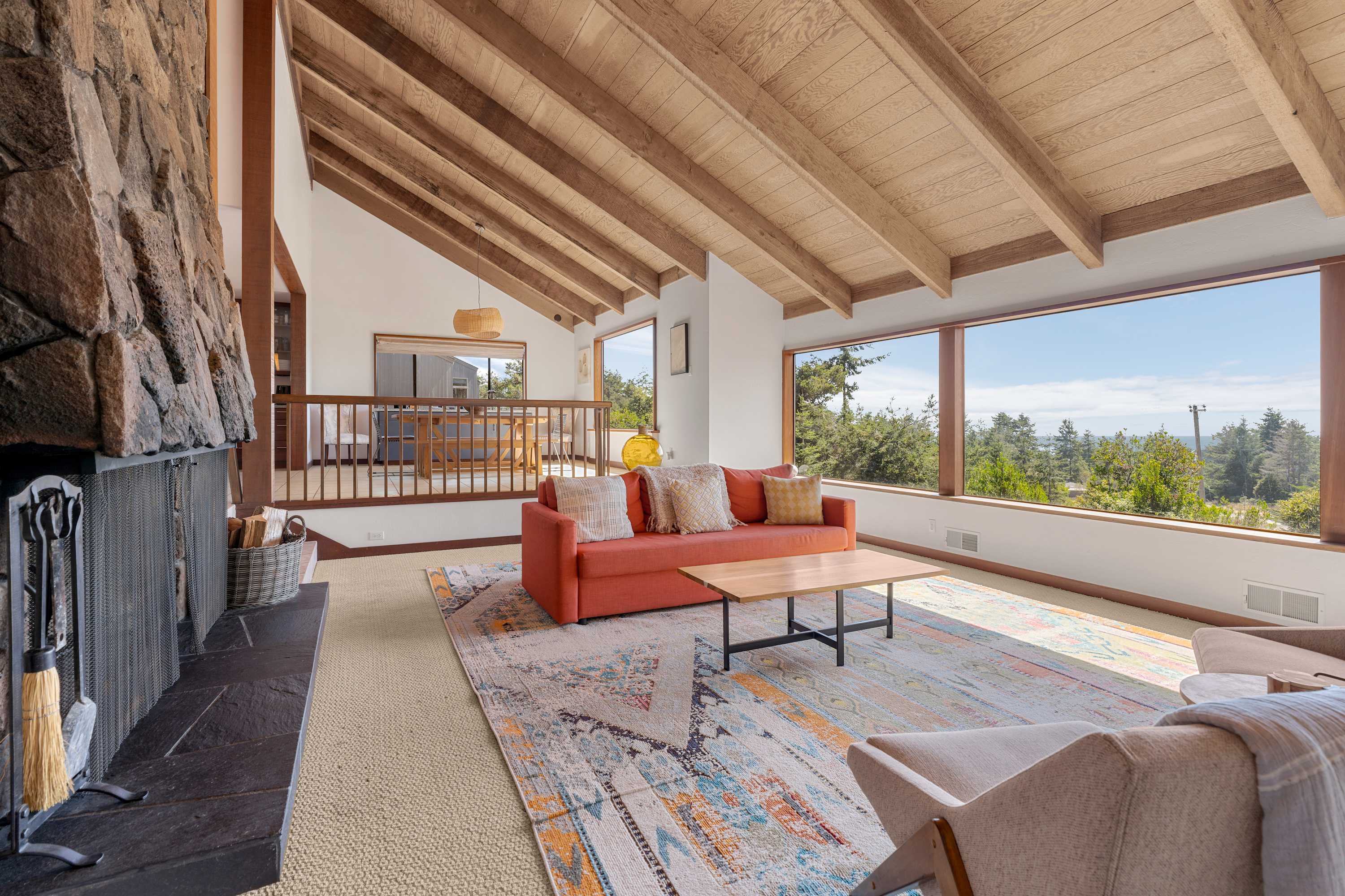 Sea Breeze opens on a vaulted great room — claim the coral sofa, face the stone hearth, and watch pines run to the Pacific.