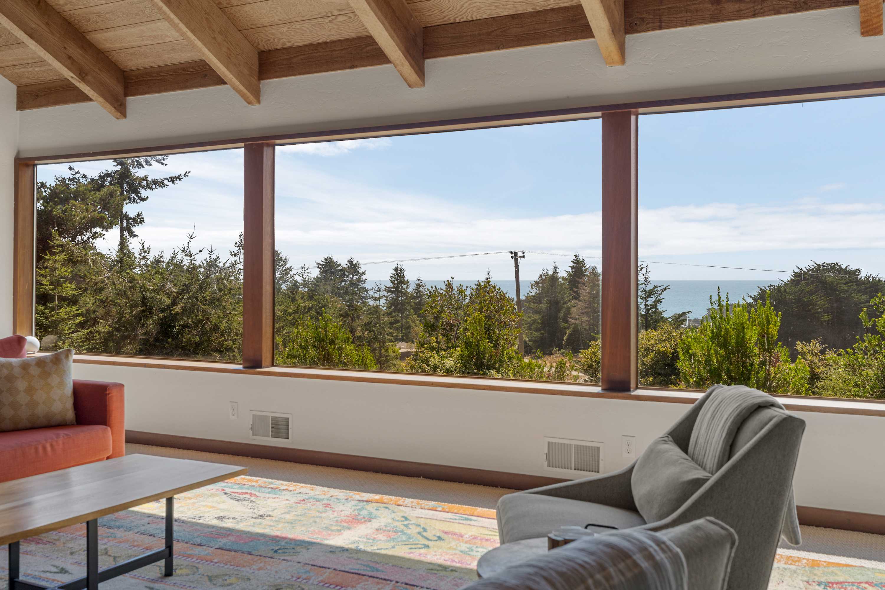 Stand at the window wall and let treetops, meadow, and a sliver of ocean fill the whole run of glass.