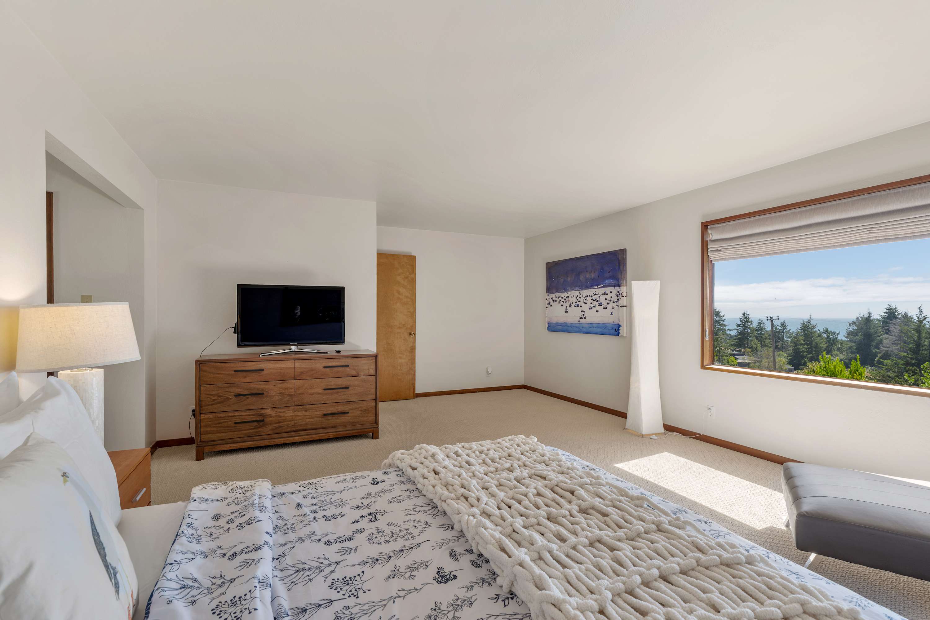 Wake in the primary to a long window of trees and water, a wall TV opposite the bed, and white linens waiting.