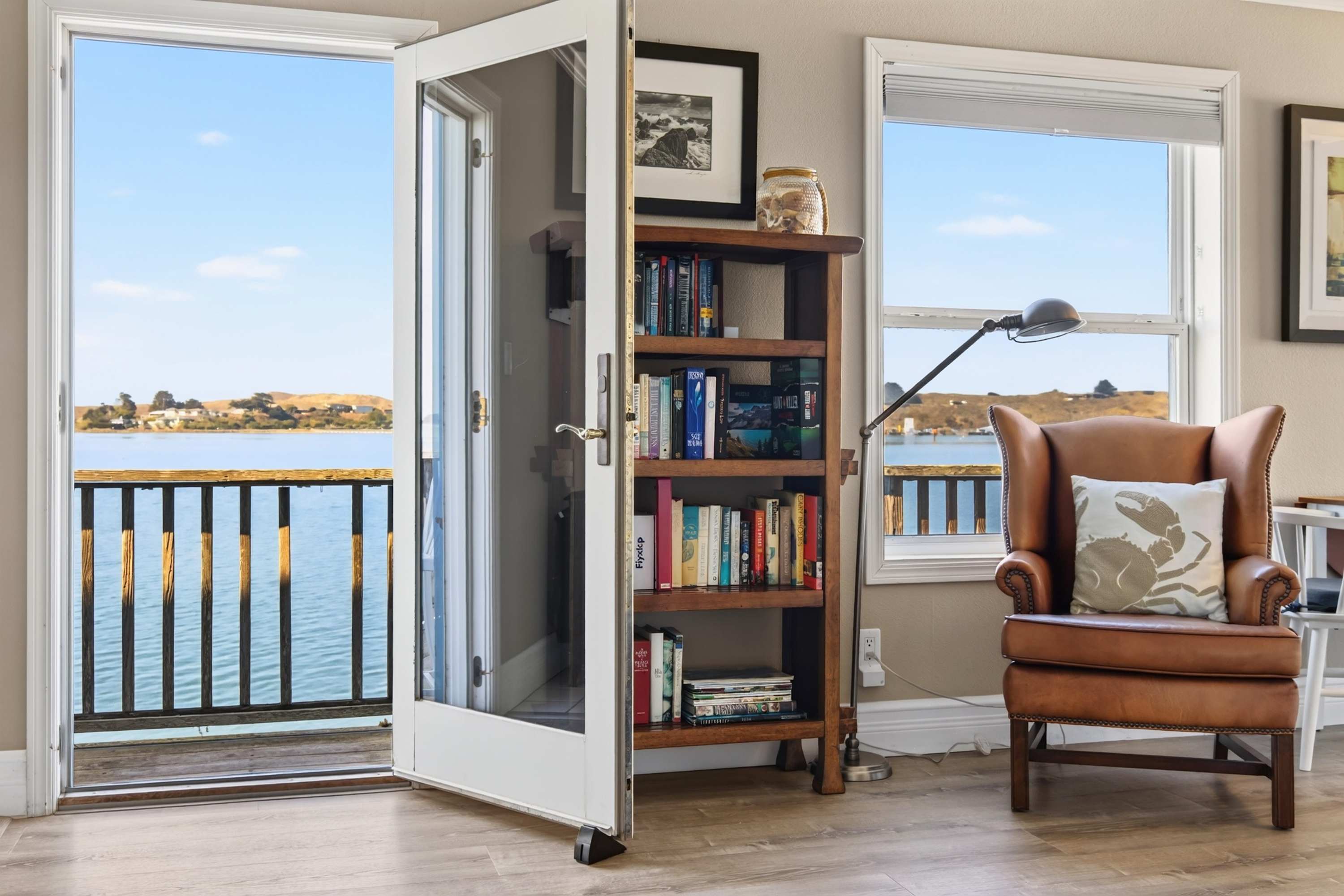 Bayside Cottage opens to the bay through a glass door — settle into the leather wingback with your crab pillow and a shelf of books.