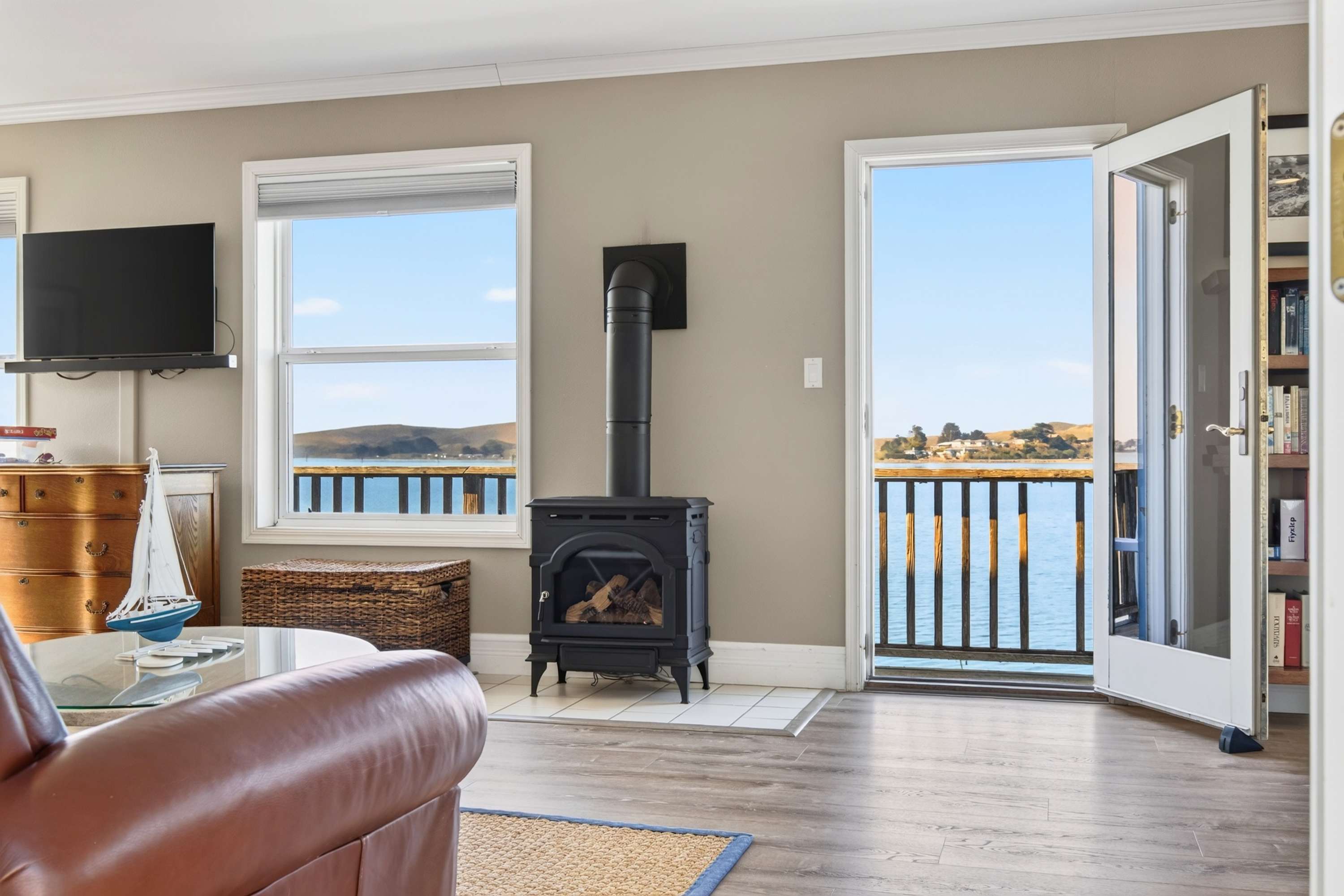 Gather around the black wood stove while calm water and golden hills fill the windows behind the sailboat on the glass coffee table.