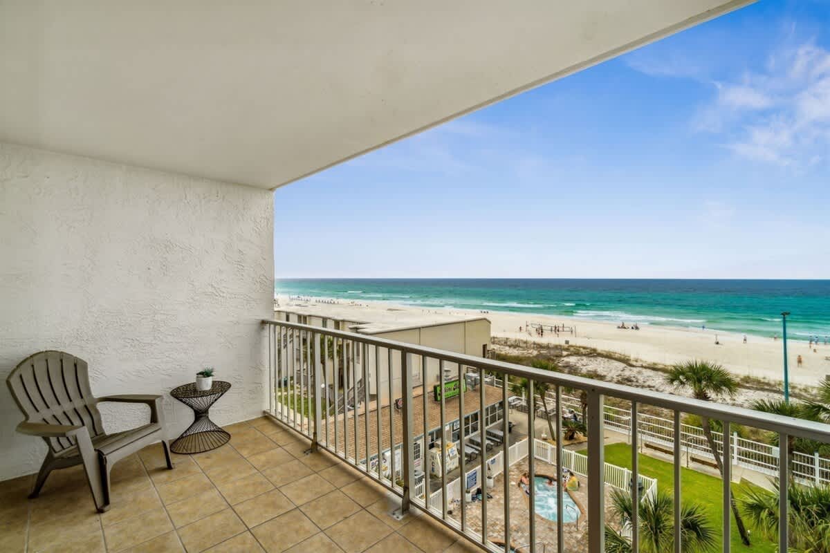 The Summit 531 – Balcony view of beach, ocean, and pool area with two chairs and a small table.