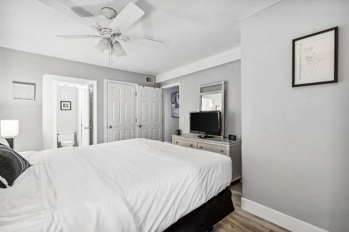 The Summit 531 – Bedroom with a queen bed, television, dresser, and a ceiling fan; light gray walls and wooden flooring.