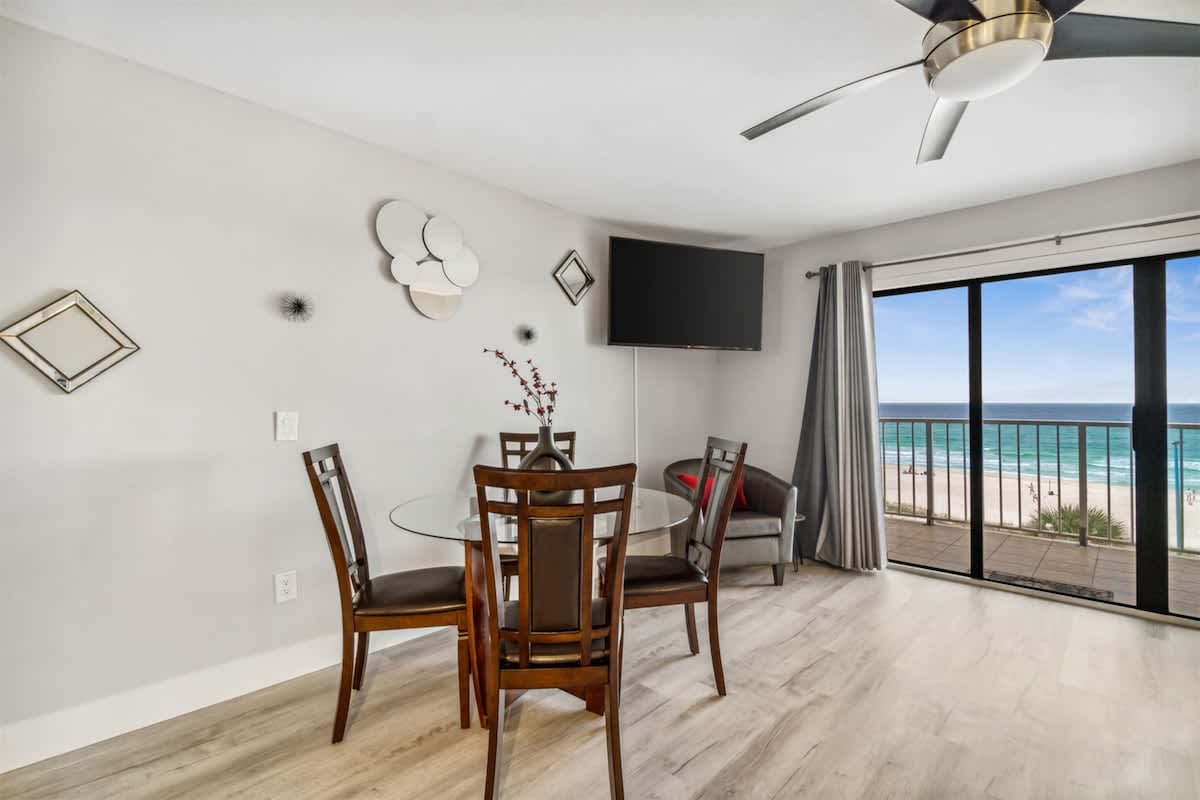 The Summit 531 – Dining area with a glass table, four chairs, a TV, and an ocean view through sliding glass doors.