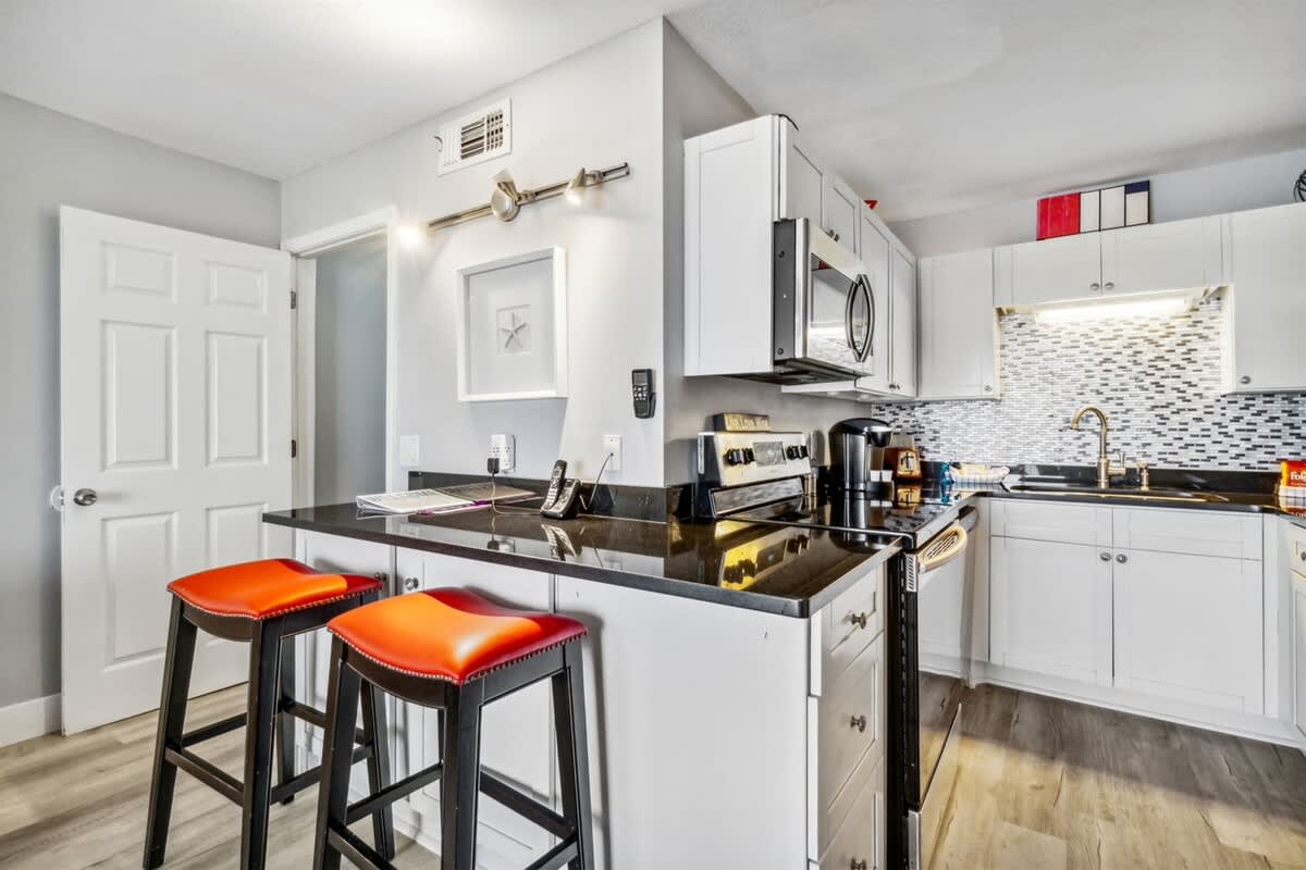 The Summit 531 – Modern kitchen with black granite countertops, stainless steel appliances, and orange bar stools.