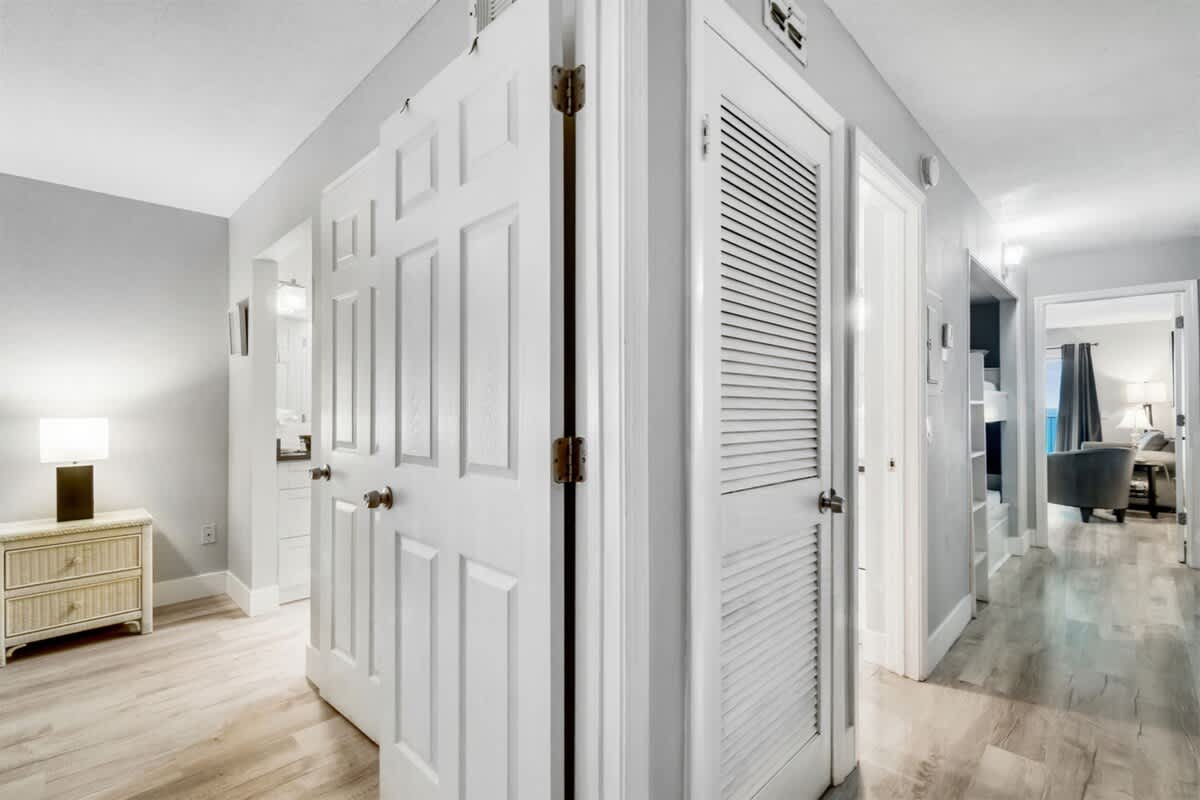 The Summit 531 – Bright hallway with white doors, light wood flooring, and a lamp on a dresser.