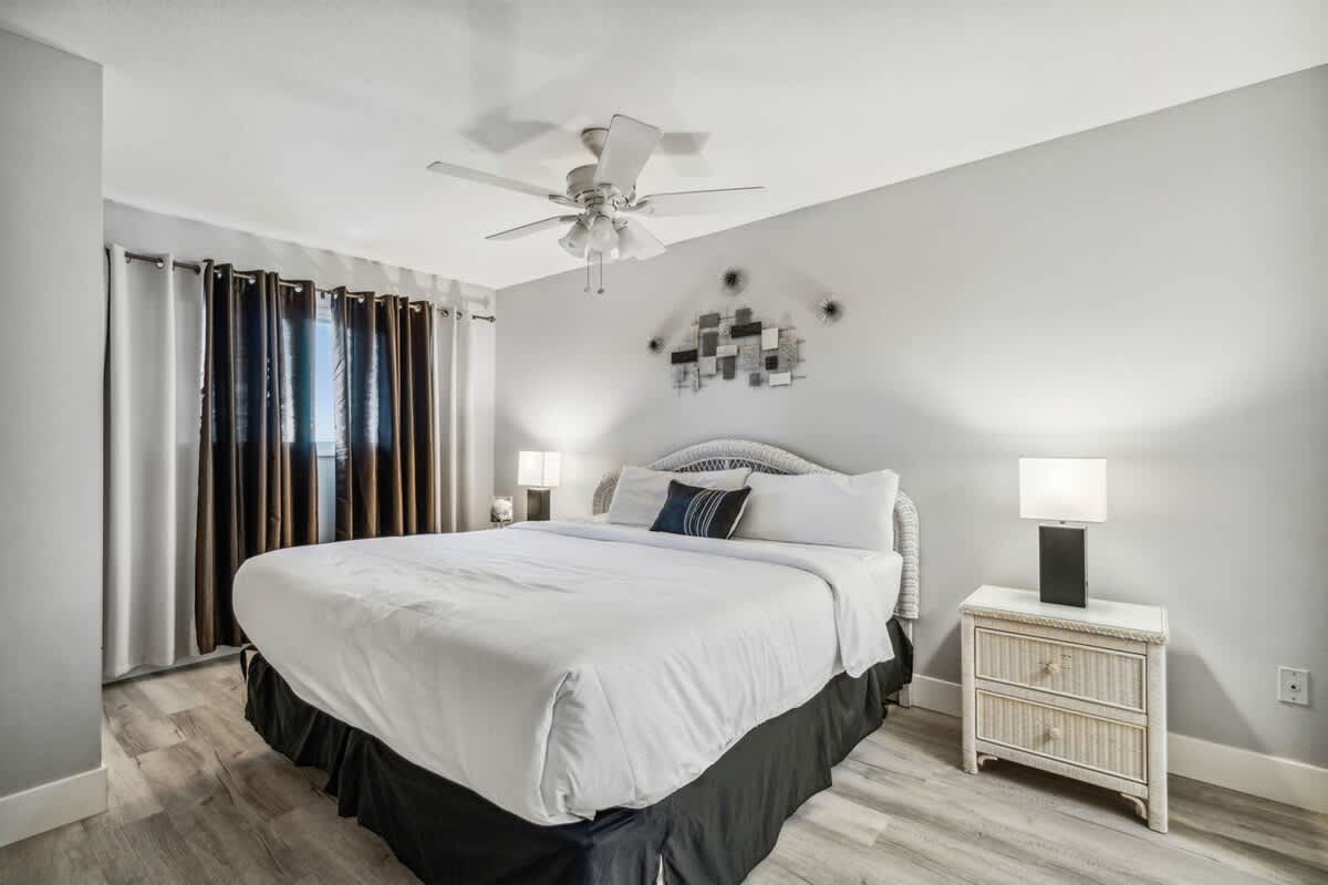 The Summit 531 – Bedroom with king-size bed, nightstands, ceiling fan, and curtains. Light wood flooring.
