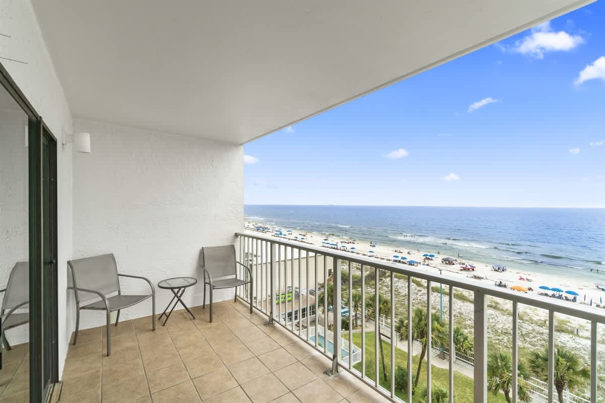 The Summit 728 – Balcony with two chairs and a table, overlooking a beach and ocean view.