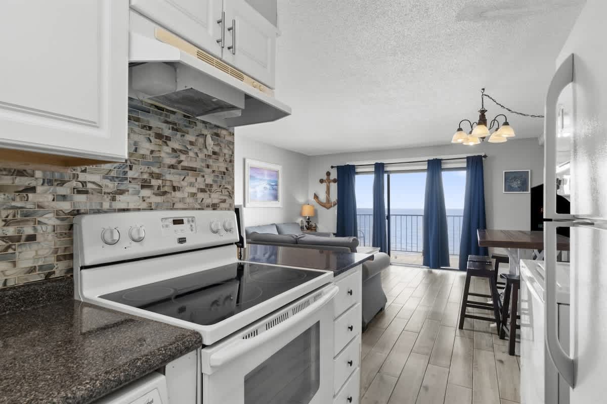 The Summit 728 – Cozy living area with ocean view, kitchenette featuring stove, and seating by large window.