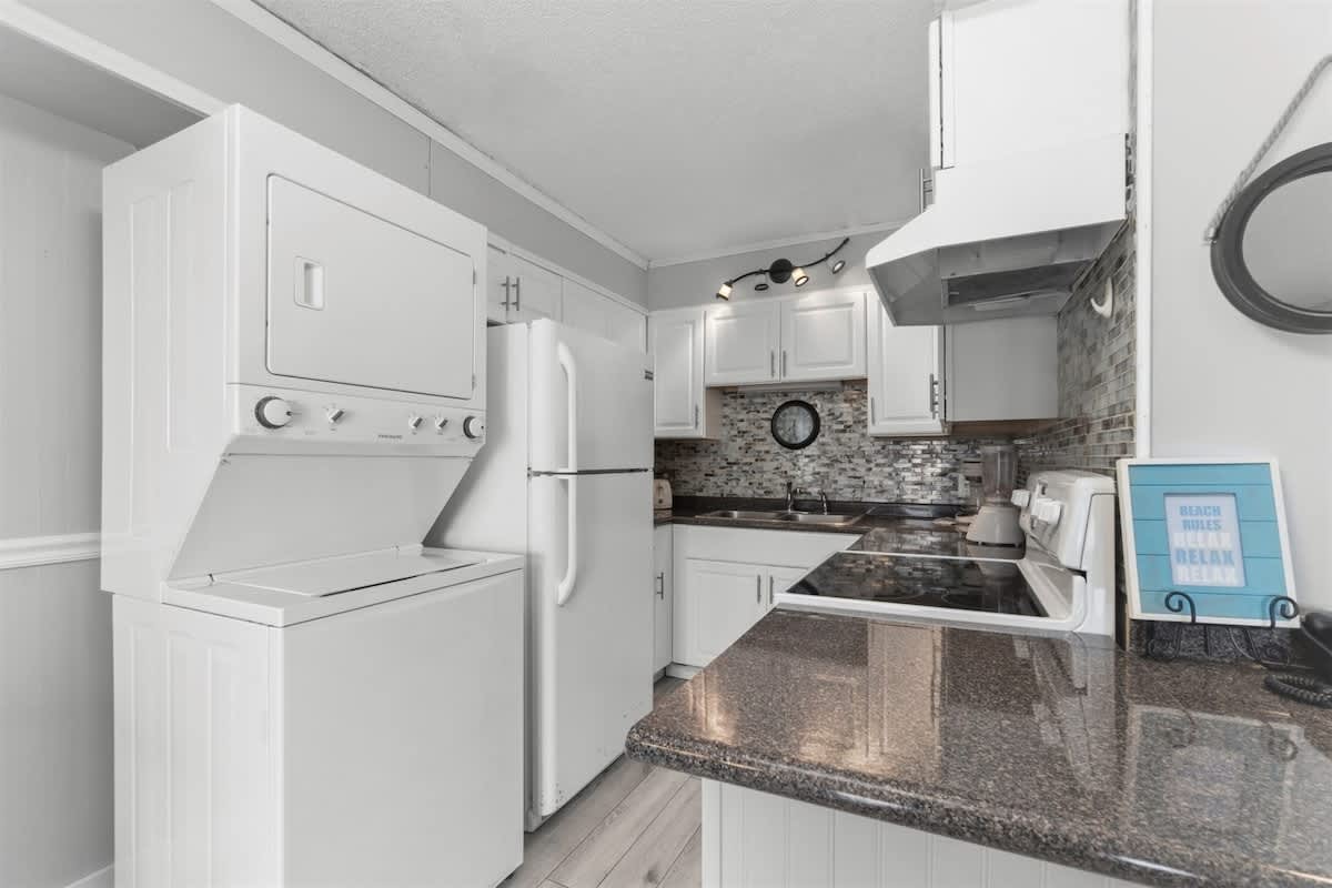 The Summit 728 – Kitchen with white appliances, stacked washer and dryer, granite countertops, and modern backsplash.