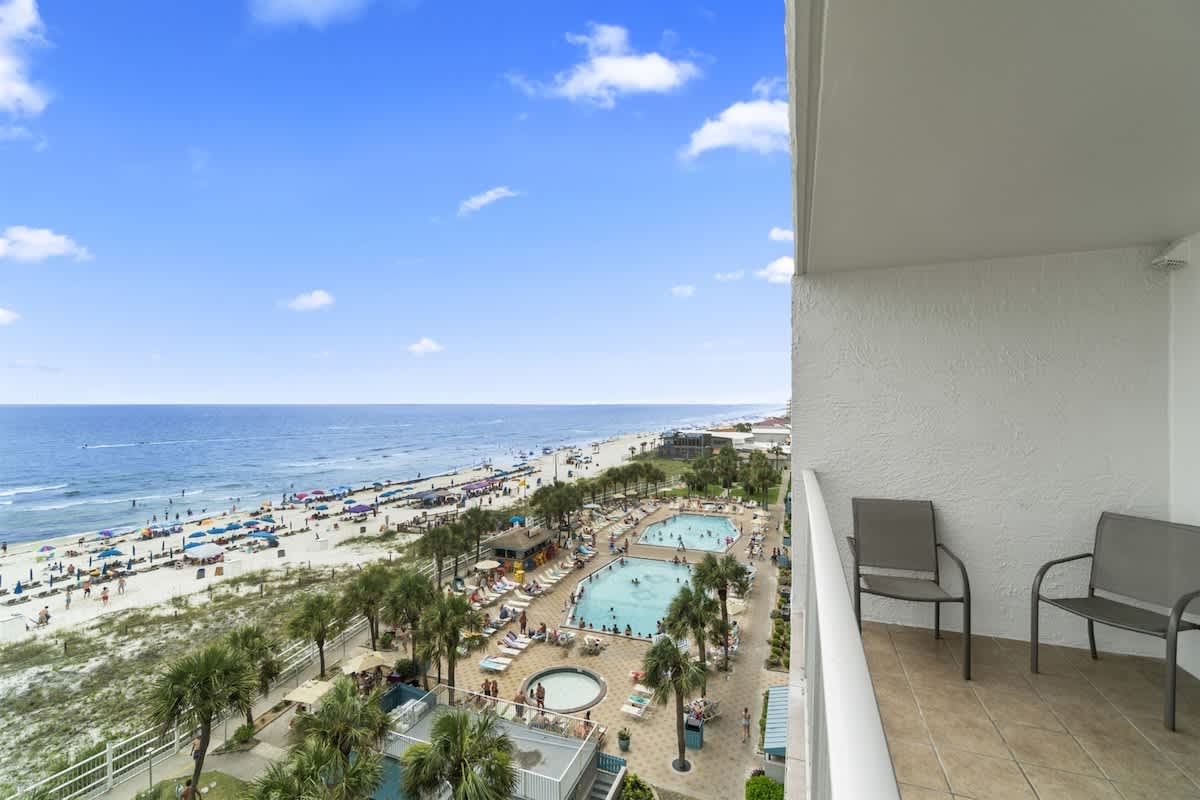 The Summit 728 – Ocean view from balcony overlooking pools and beach, with chairs on the terrace.