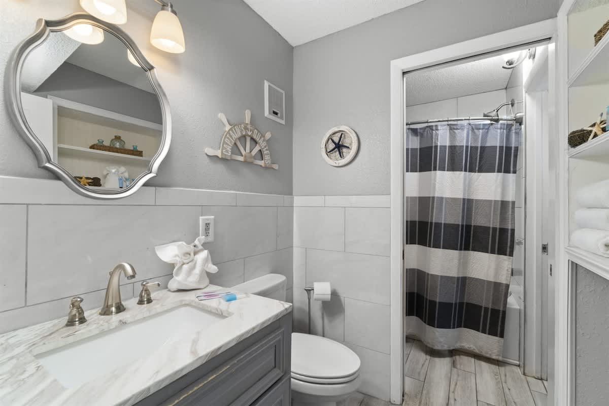 The Summit 728 – Bathroom with a marble vanity, mirror, striped shower curtain, and decorative nautical elements.