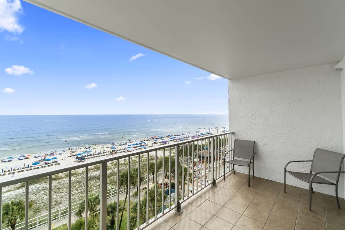 The Summit 728 – Balcony with two chairs overlooking a beach, ocean, and colorful umbrellas.