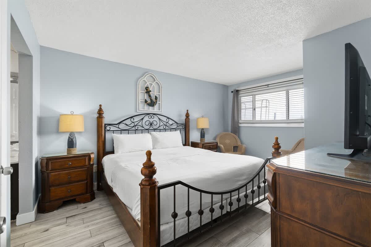 The Summit 728 – Bedroom with a king bed, two nightstands, a chair, and a window with blinds.