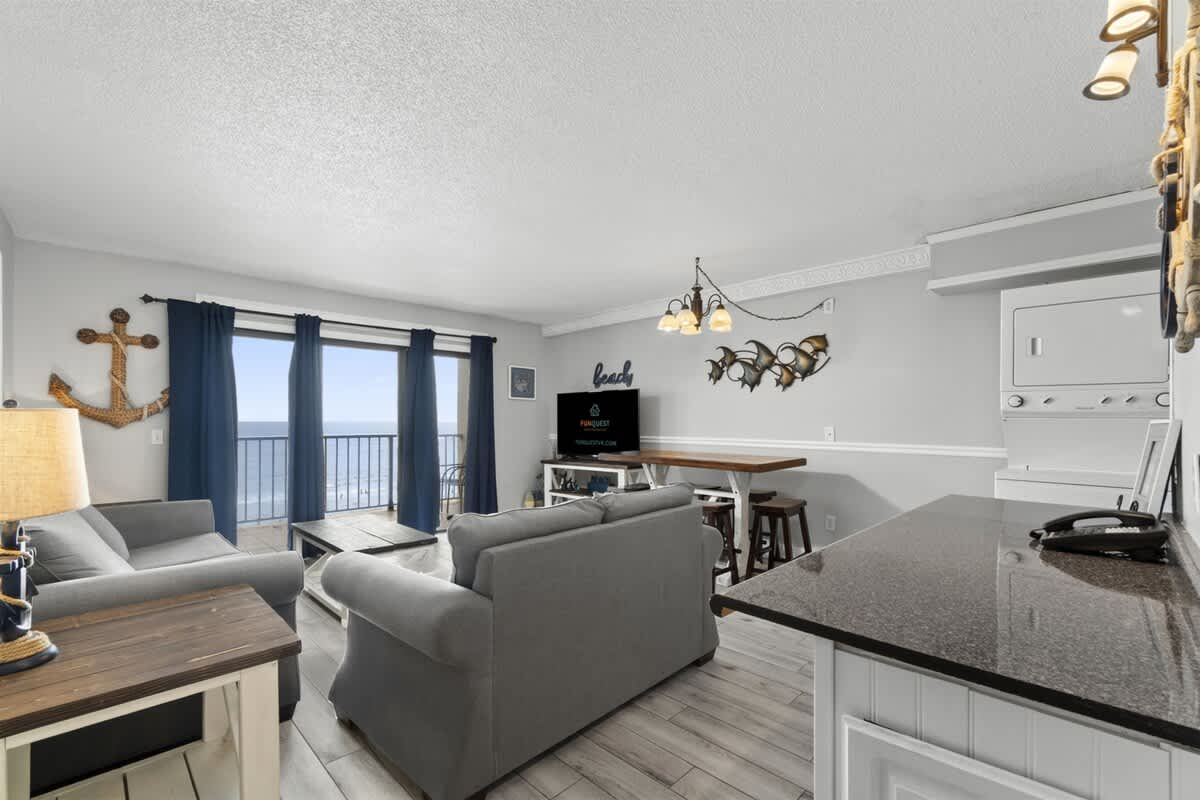 The Summit 728 – Living room with ocean view, gray sofas, dining area, and a TV.