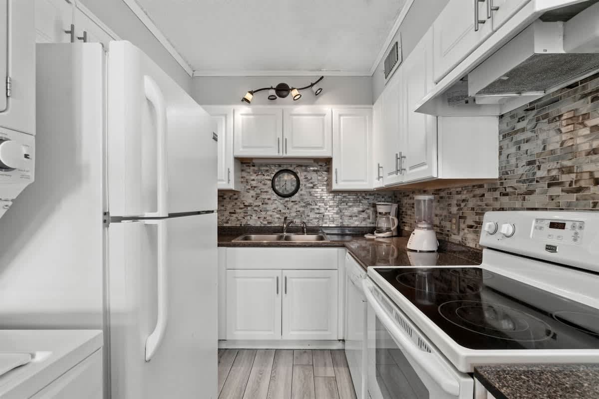 The Summit 728 – Modern kitchen with white appliances, granite countertops, and mosaic backsplash.