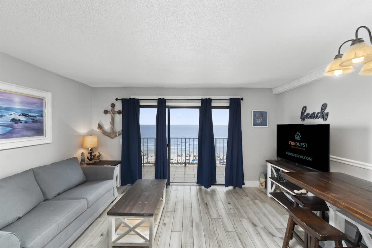The Summit 728 – Living room with gray couch, wooden table, and ocean view through sliding glass doors.