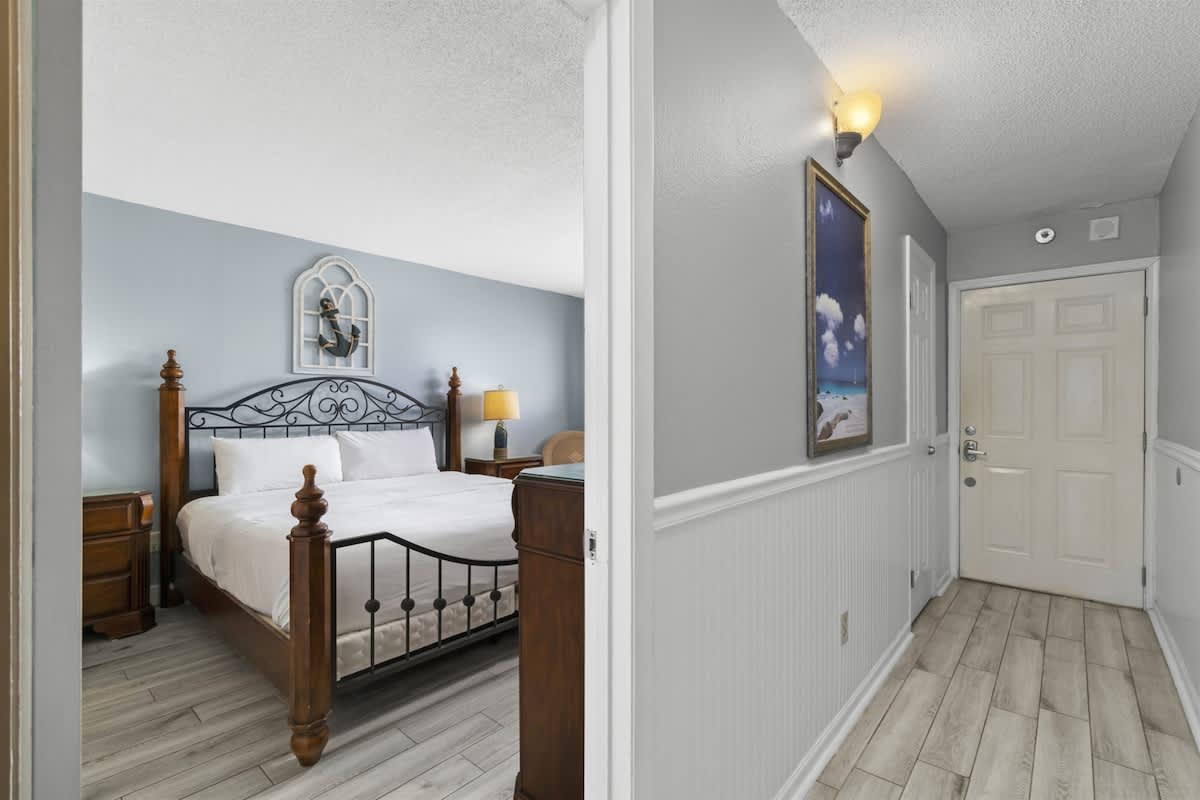 The Summit 728 – Bedroom with a wooden bed frame, nightstands, decorative wall art, and an entryway visible.