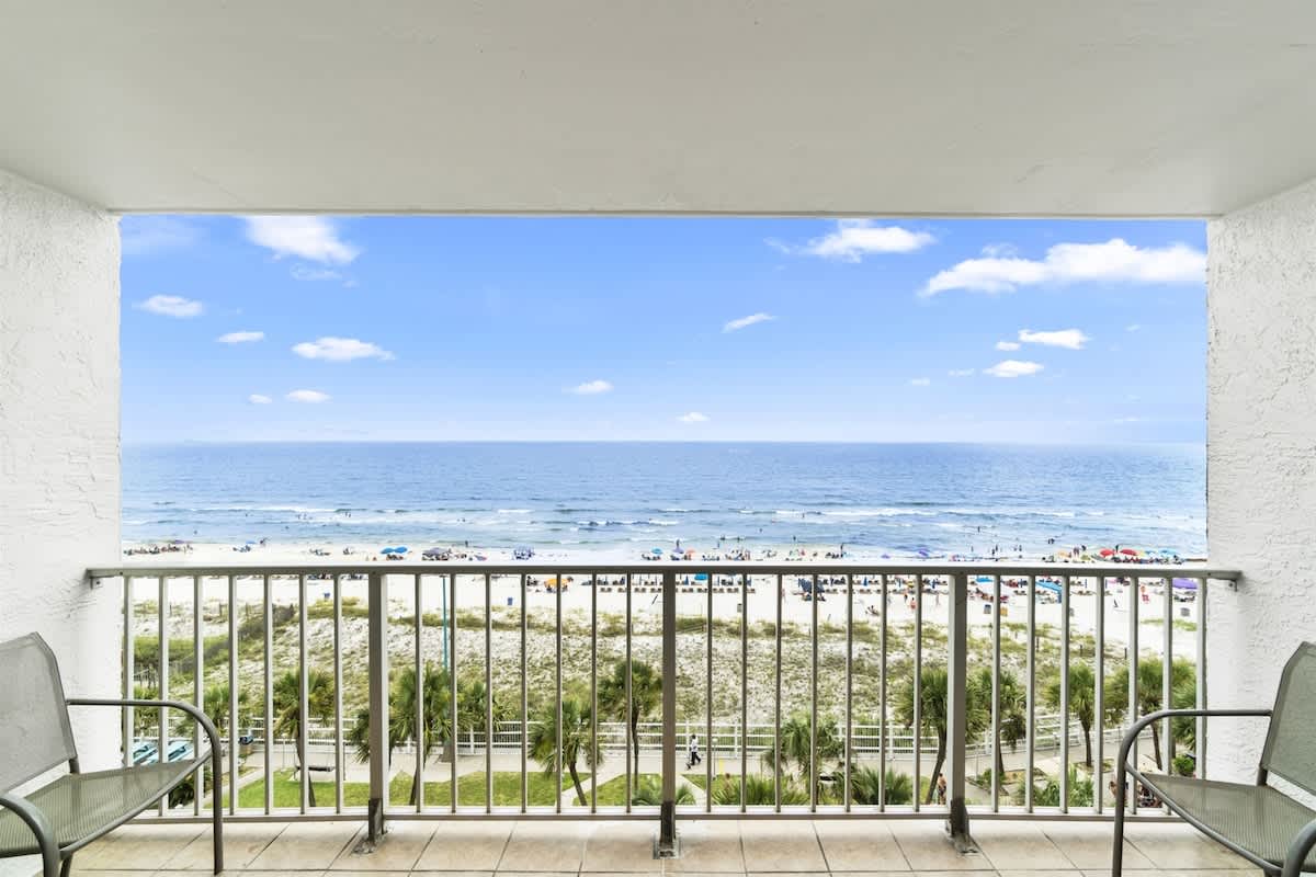 The Summit 728 – Balcony view overlooking beach, ocean, and clouds with two chairs in foreground.
