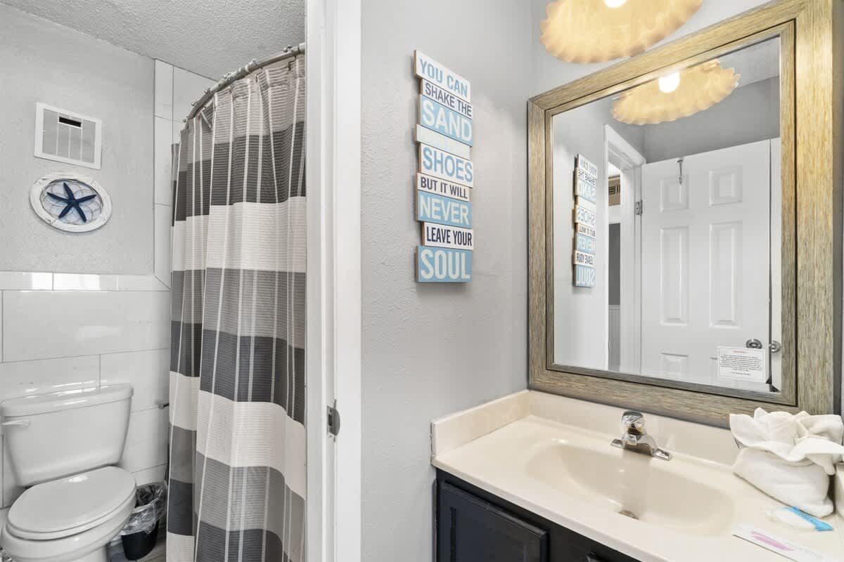 The Summit 728 – Bathroom featuring a toilet, sink, mirror, and a shower curtain with striped pattern.