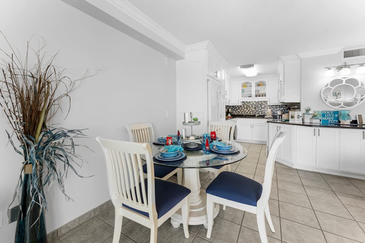 The Summit 1130 – Dining area with round glass table, white chairs, and open kitchen view featuring dark countertops and modern cabinetry.
