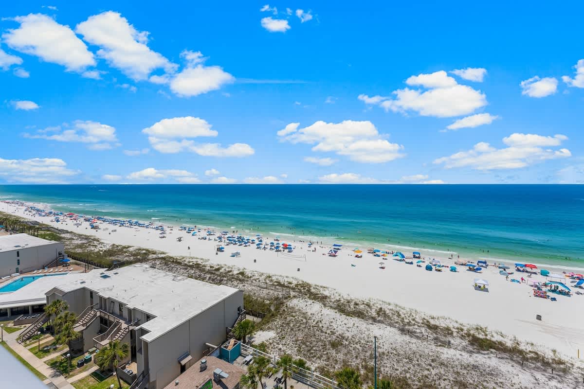 The Summit 1130 – Beach view from a balcony overlooking white sand, ocean, and blue sky with scattered clouds.