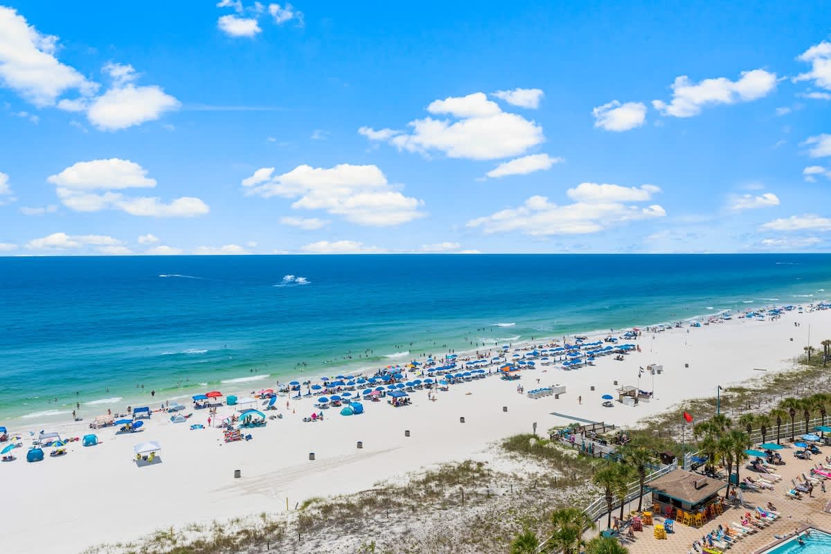 The Summit 1130 – View of a sandy beach with umbrellas, lounge chairs, and ocean stretching into the horizon.