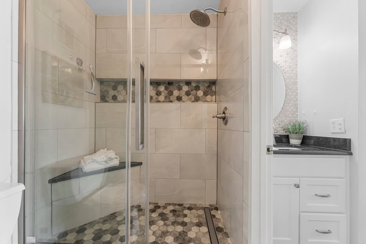 The Summit 1130 – Modern bathroom featuring a glass shower, hexagonal tile flooring, and a vanity with a circular mirror.