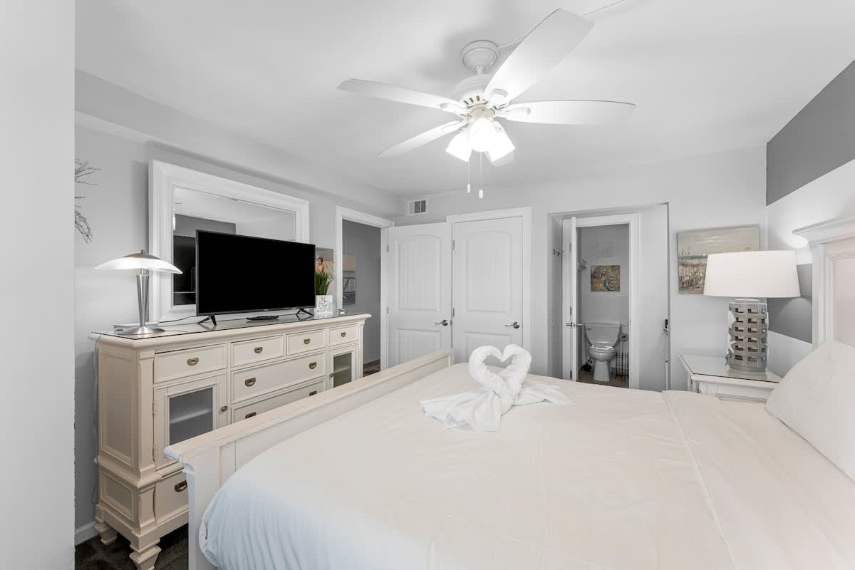 The Summit 1130 – Bedroom with a king bed, TV, dresser, and adjoining bathroom door.