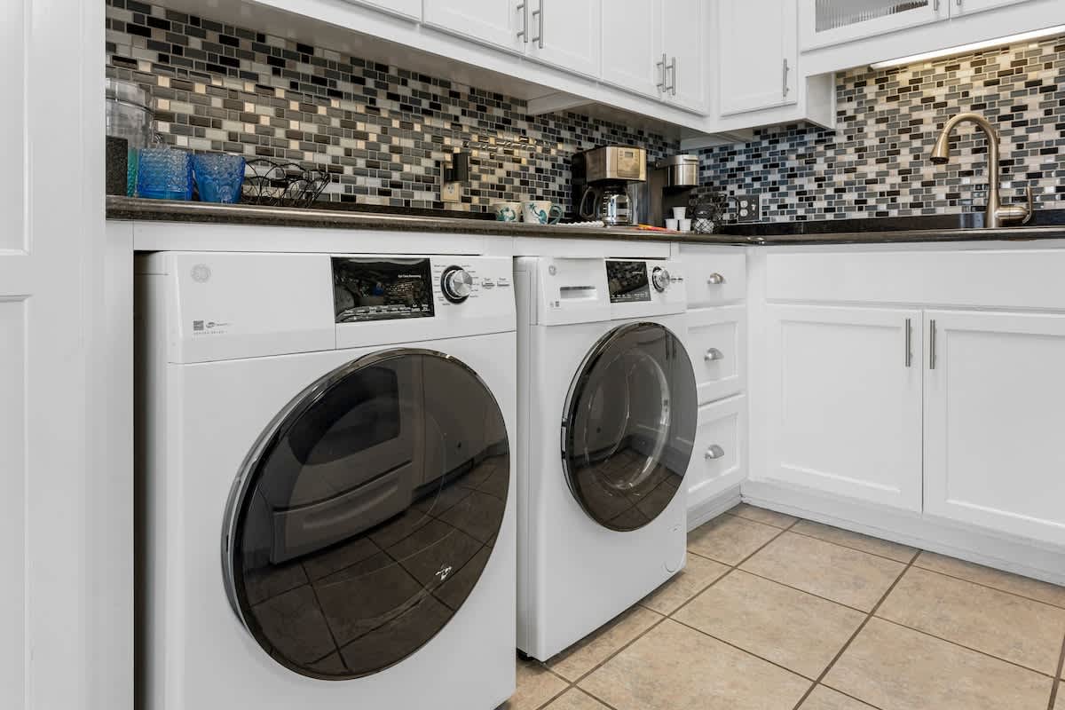 The Summit 1130 – Laundry area with white washer and dryer, granite countertop, and mosaic tile backsplash.