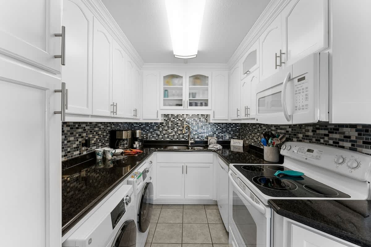 The Summit 1130 – Modern kitchen with white cabinets, black countertops, stainless steel appliances, and a tile backsplash.