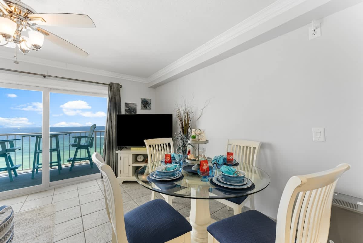 The Summit 1130 – Dining area with round glass table, four chairs, and ocean view through sliding glass doors.