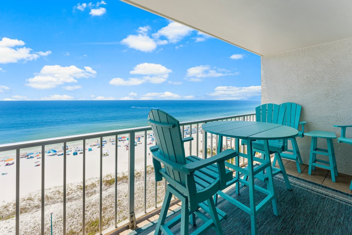 The Summit 1130 – Balcony with turquoise furniture overlooking beach and ocean under a bright blue sky.
